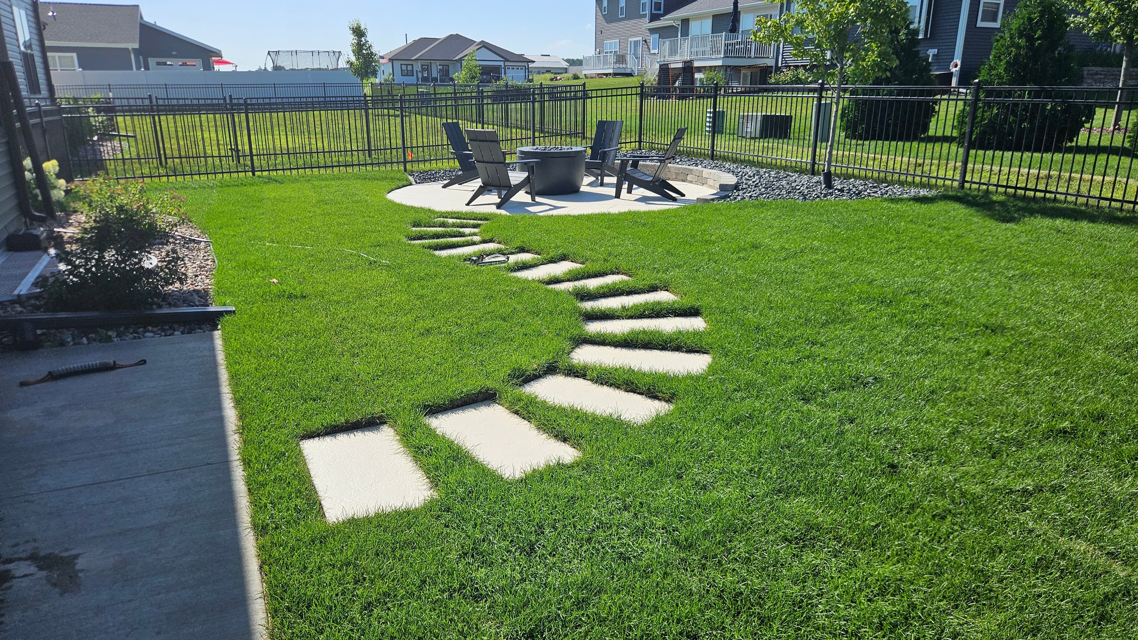 Complete backyard landscape design in Baraboo WI showing flagstone walkway across lawn to circular fire pit patio with decorative rock border and Adirondack chairs