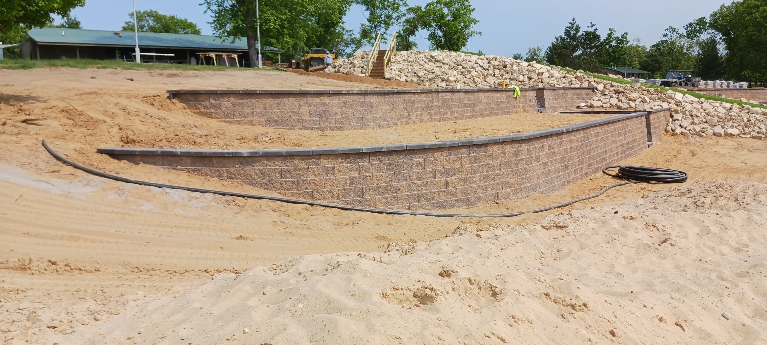 Multi-tiered curved retaining walls under construction showing professional drainage pipe installation and proper base preparation in Central Wisconsin
