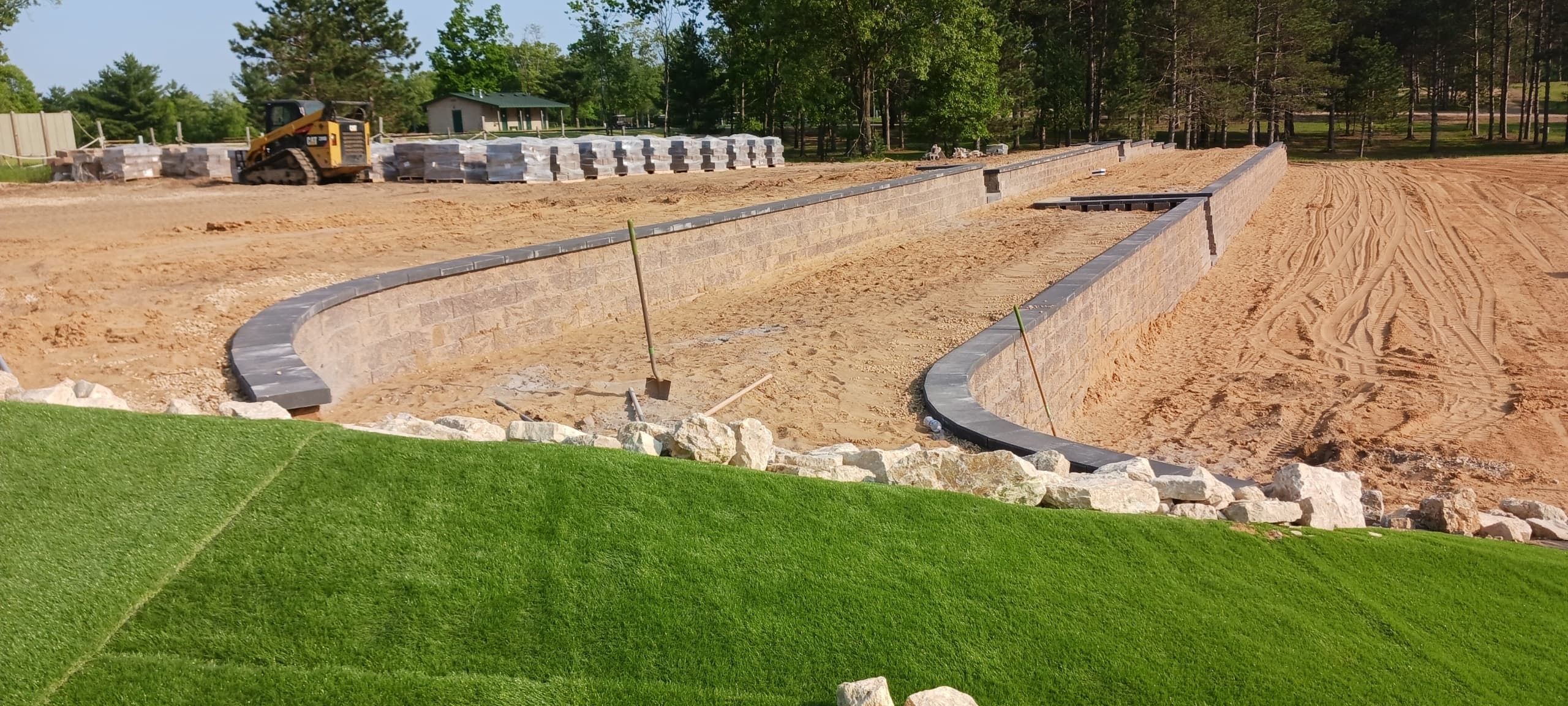 Completed curved retaining wall sections with professional sod installation, decorative boulder placement, and natural stone accents in Central Wisconsin