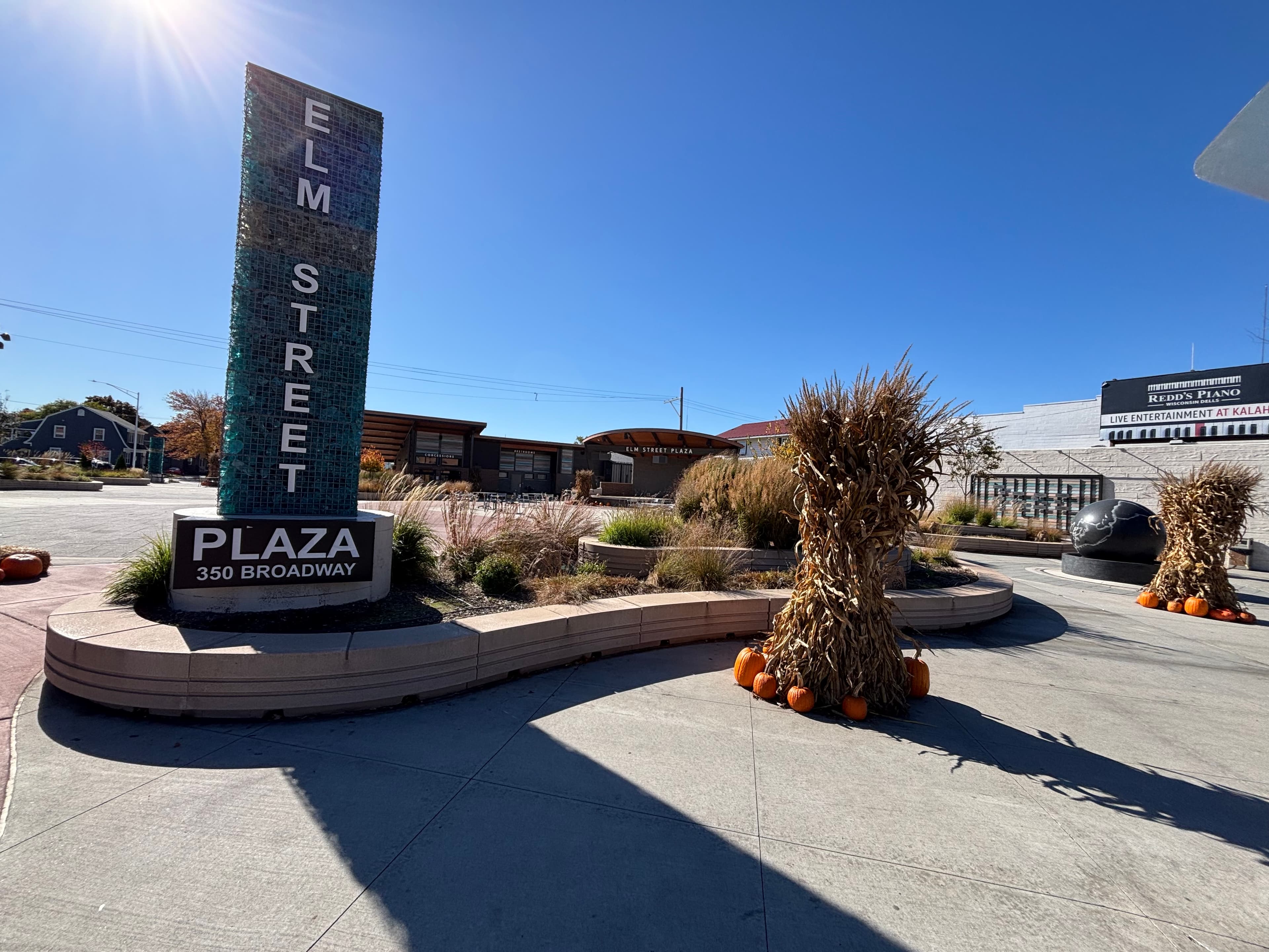Elm Street Plaza monument sign with curved concrete planters featuring ornamental grasses and seasonal corn stalk decorations in downtown Wisconsin Dells