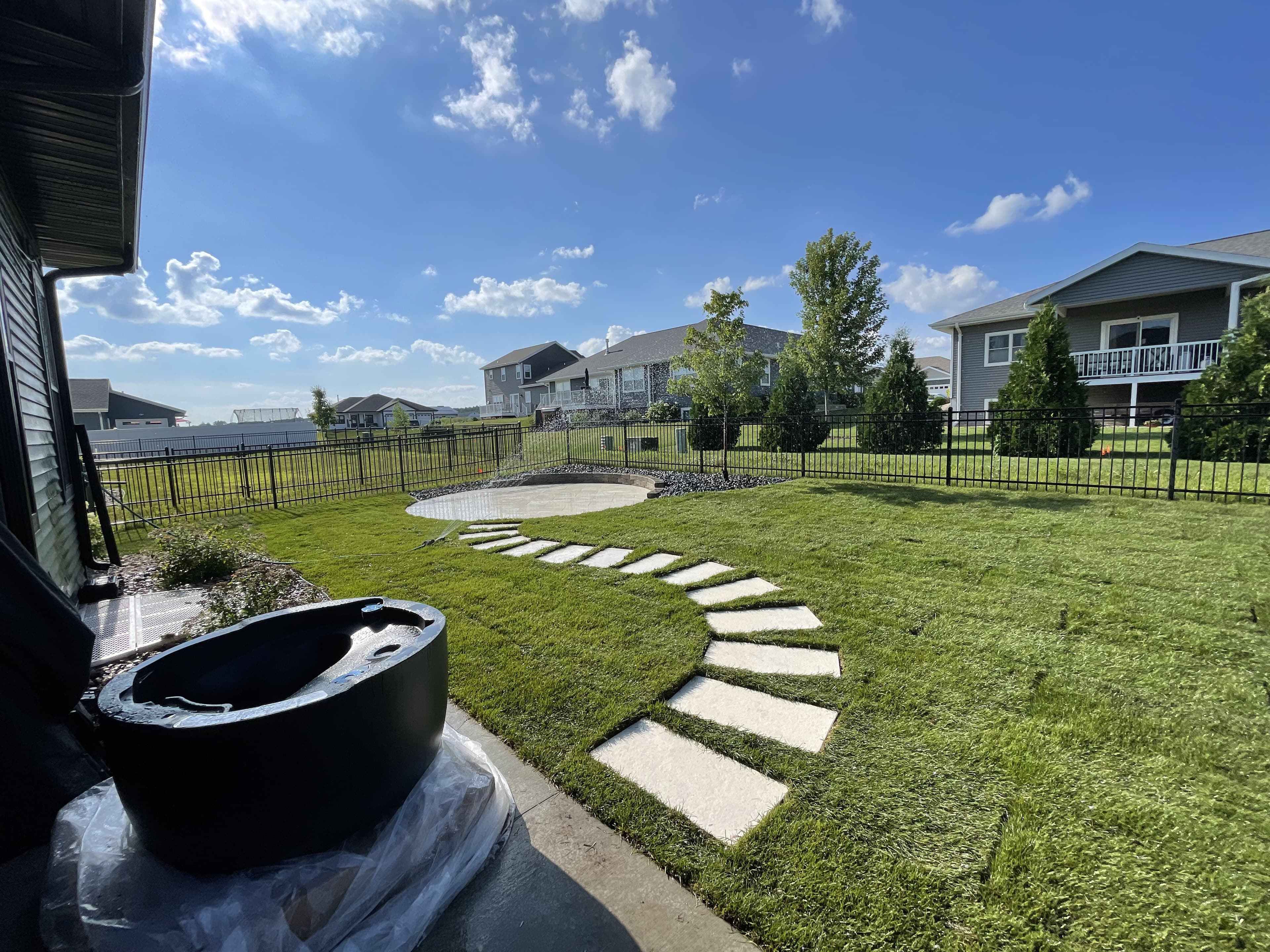Flagstone stepping stone pathway through green lawn in Baraboo Wisconsin leading to fire pit with black metal fire pit visible on patio