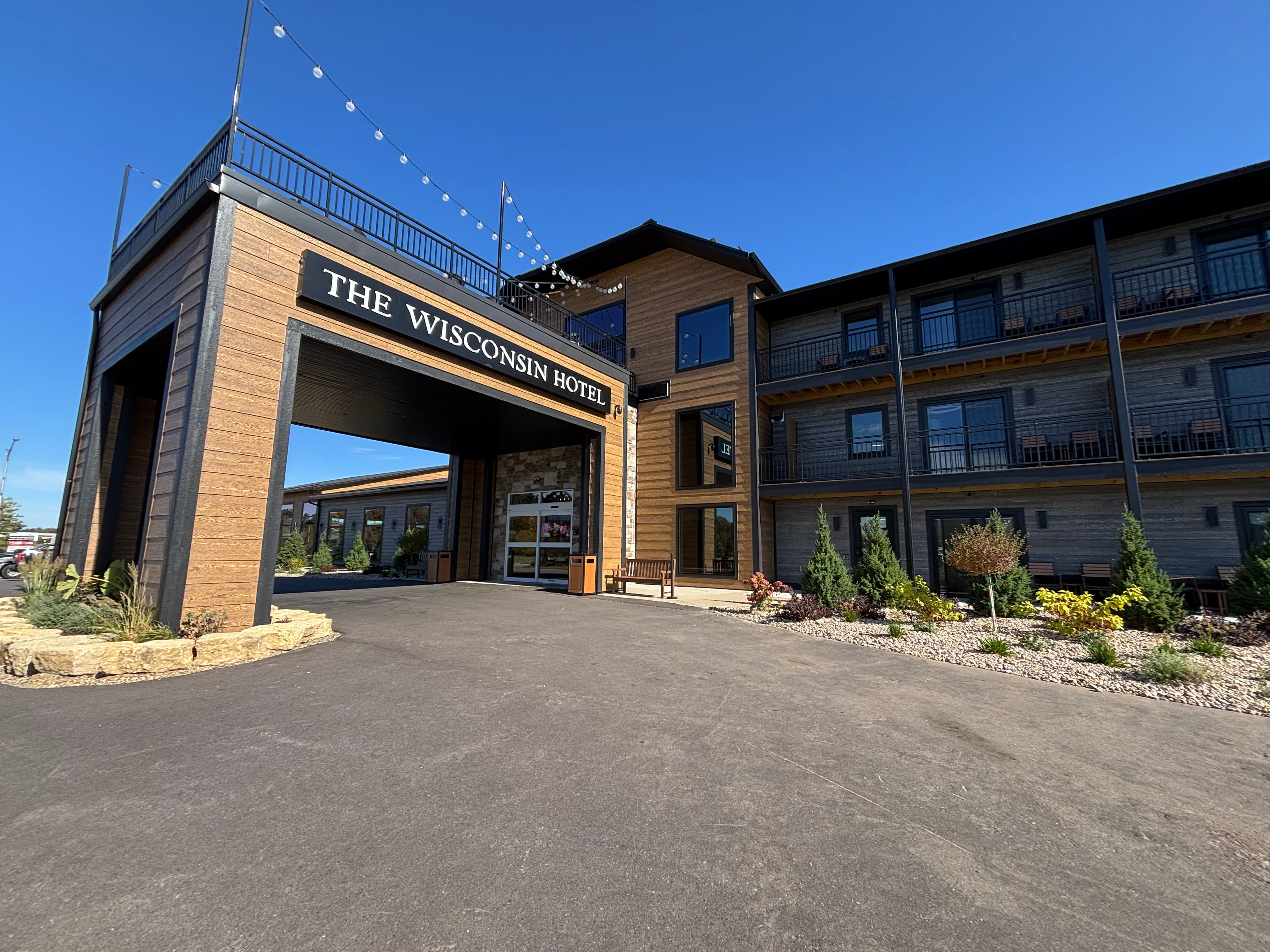 Completed entrance landscaping at The Wisconsin Hotel featuring columnar evergreens, ornamental grasses, and professional commercial plantings with decorative rock mulch